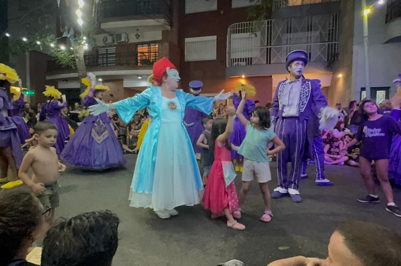 Murga performers wearing colorful purple, yellow, and blue costumes.